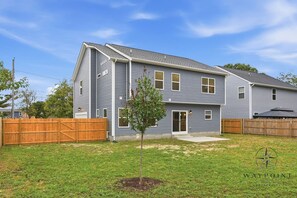A two-story residential house with a front yard, a wooden fence, and a small tree. - Modern Coastal Retreat 4BR | Near Base & Fishing Pier - 30 Day Minimum Stay (Norfolk)