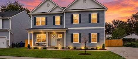A two-story residential house with a front porch, a garage, and a well-maintained lawn.