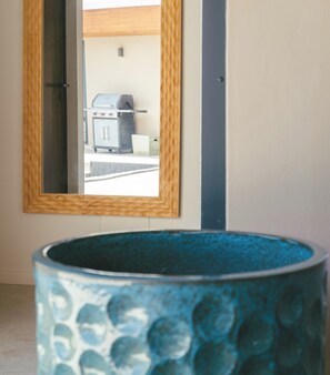 Ein Badezimmer mit einer blauen Badewanne mit Struktur, einem spiegeln Spiegel mit Holzrahmen und Blick auf einen Grill draußen.