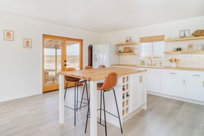 A modern kitchen with white cabinets, a wooden island, and bar stools. - Loma Vista | Pool | Hot Tub | Casita I Stargazing I 5 Acres I Wide-Open Views (Joshua Tree)