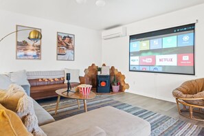A modern living room with a fireplace, a projector screen displaying streaming apps, and a cozy seating area. - Loma Vista | Pool | Hot Tub | Casita I Stargazing I 5 Acres I Wide-Open Views (Joshua Tree)