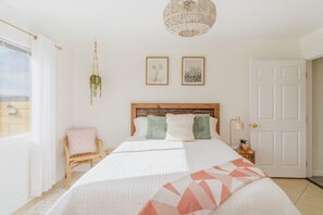 A bedroom with a bed, a hanging plant, two framed pictures, a door, and a window. - Loma Vista | Pool | Hot Tub | Casita I Stargazing I 5 Acres I Wide-Open Views (Joshua Tree)