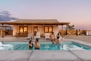 A pool area with lounge chairs, a wooden deck, and a building with string lights. - Loma Vista | Pool | Hot Tub | Casita I Stargazing I 5 Acres I Wide-Open Views (Joshua Tree)