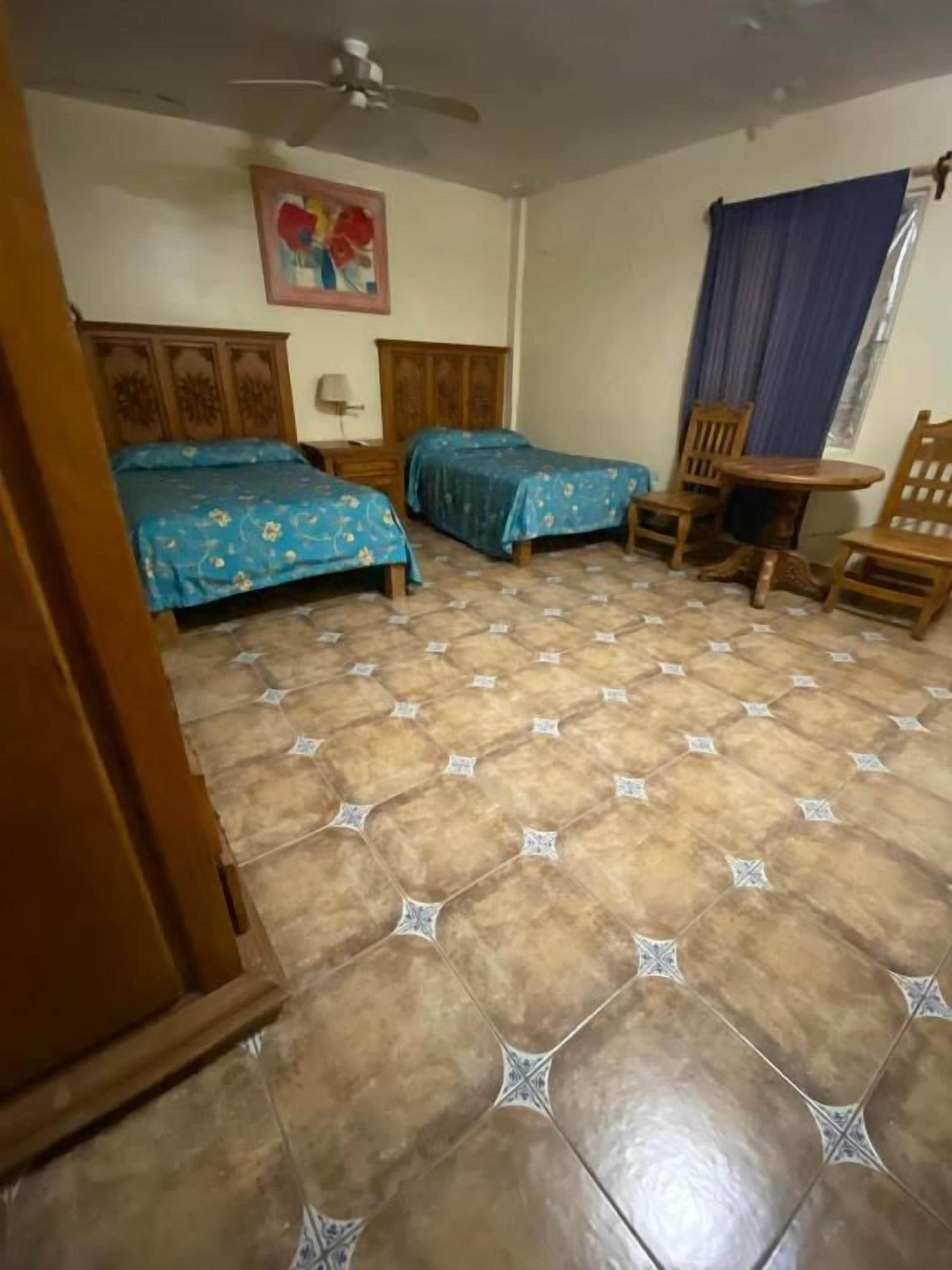 A room with two beds, a ceiling fan, a table, and chairs.