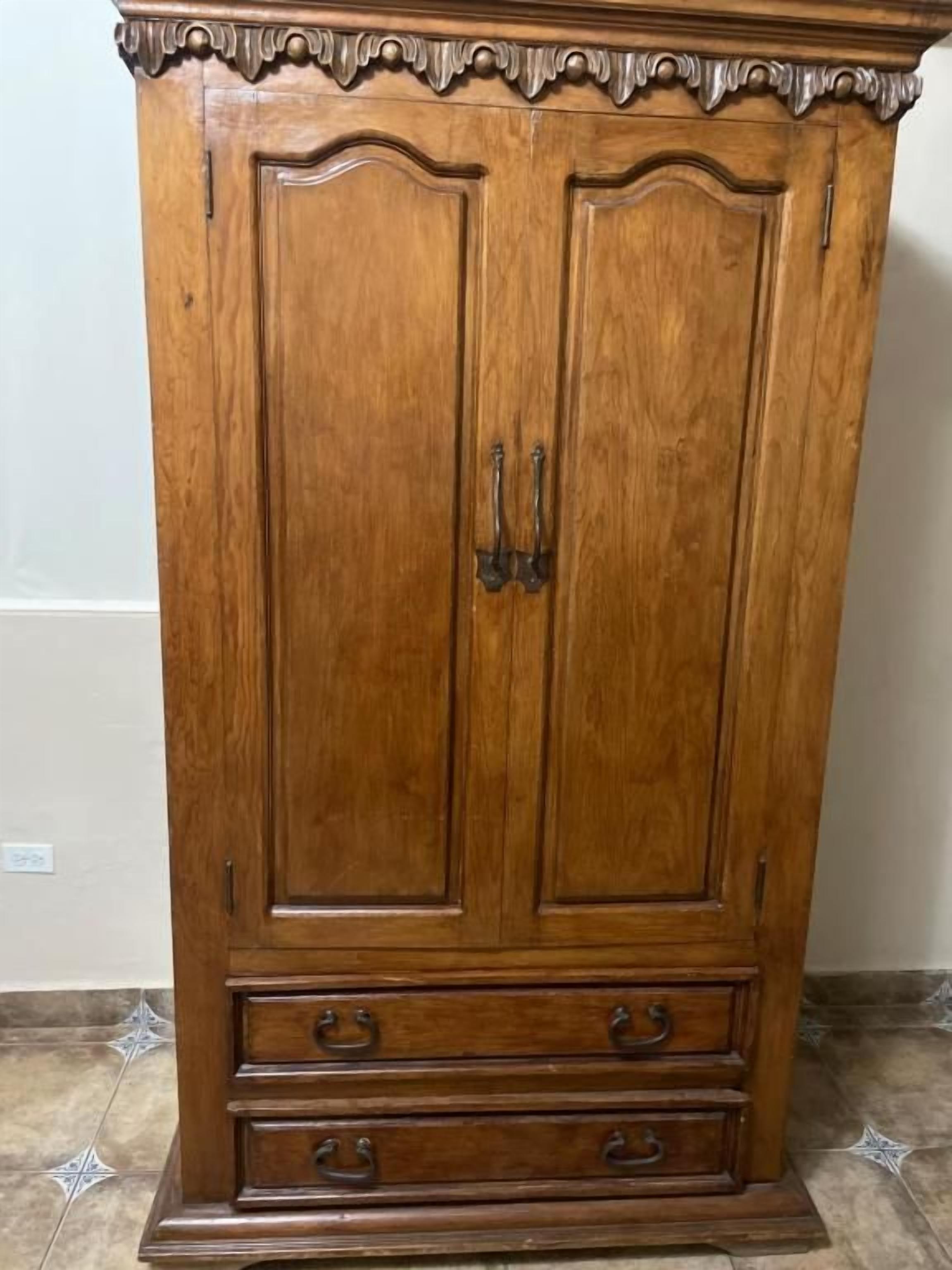 A wooden wardrobe with two doors and three drawers, featuring ornate handles and a decorative top.
