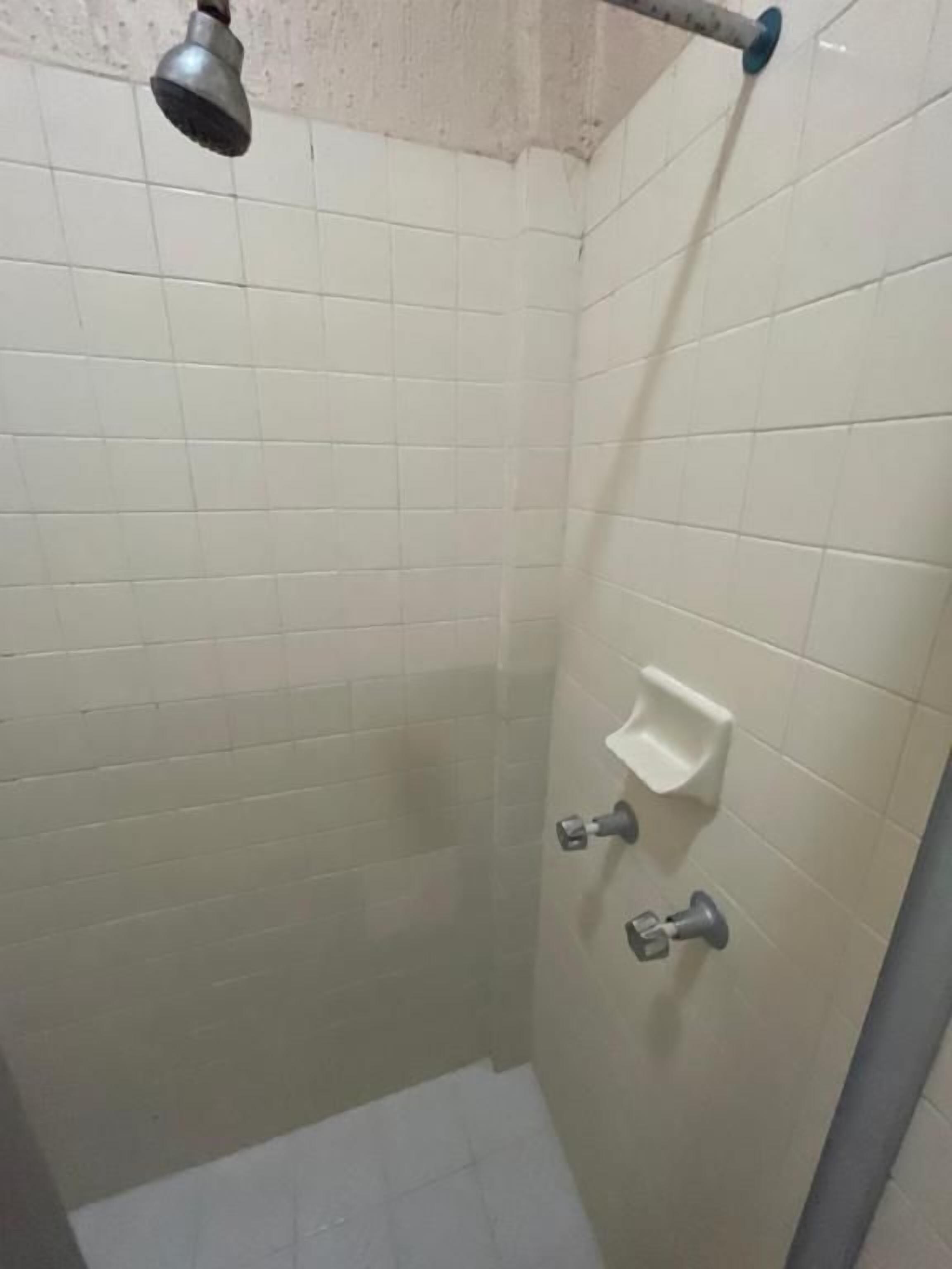 Un espacio de ducha pequeño y cerrado con azulejos blancos, un cabezal de ducha de mano y un jabonera.