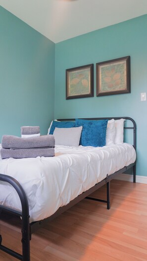 Una cama con estructura metálica, ropa de cama blanca y varias almohadas en una habitación con paredes verde azulado.
