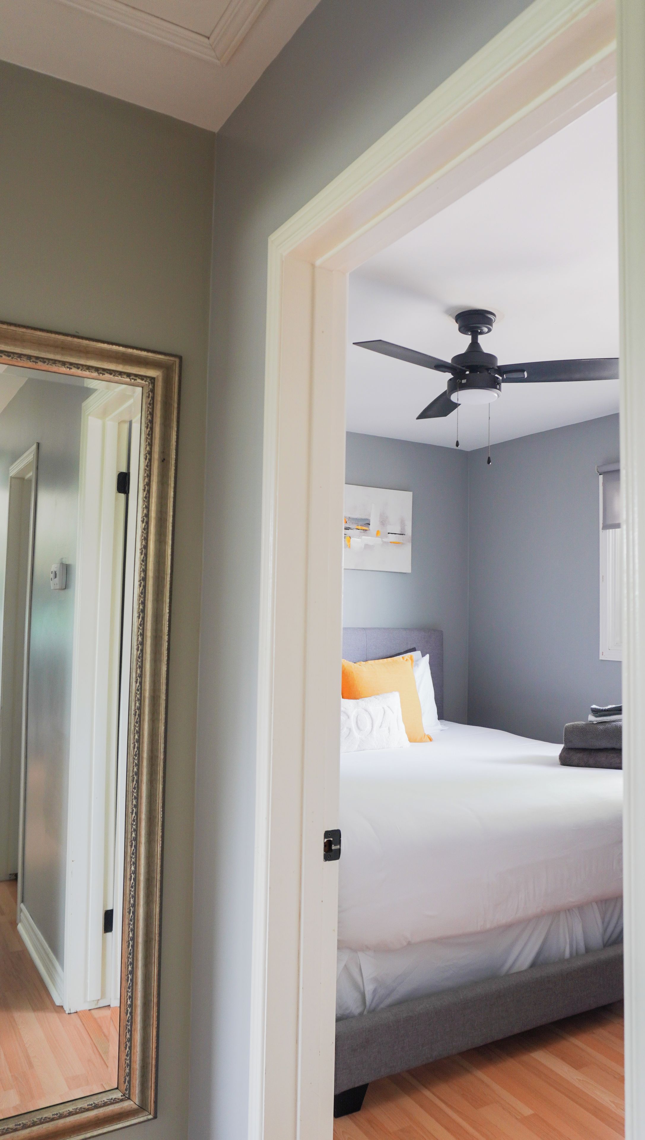 A bedroom with a bed, a ceiling fan, a wall-mounted artwork, and a door leading to another room.