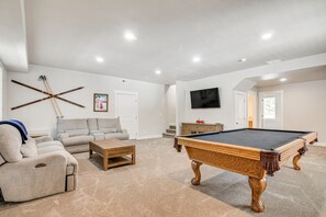Ein Wohnzimmer mit Billardtisch, einer Couch, einem Couchtisch und einem Fernseher.