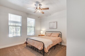 A bedroom with a bed, a ceiling fan, two windows, a nightstand, and a wall-mounted light. - High Country Hideaway (Duck Creek Village)