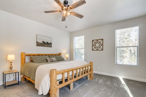 A bedroom with a wooden bed, a ceiling fan, a nightstand with a lamp, and a window with blinds. - High Country Hideaway (Duck Creek Village)