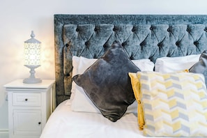 Ein Bett mit einer gesteppten Kopfteil, weißer Bettwäsche und mehreren Kissen in verschiedenen Farben.