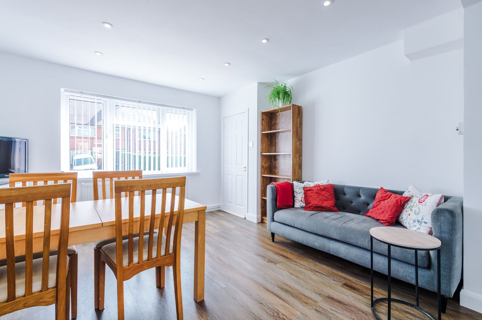 A modern living room with a grey sofa, wooden dining table, and chairs.