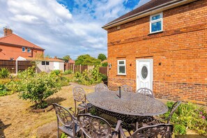 A brick house with a garden, a metal table with chairs, and a wooden fence. - Nottingham | Modern Home | Free Parking | Sleeps 5 (Beeston)