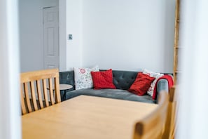 A room with a grey sofa, a wooden chair, and a small round table. - Nottingham | Modern Home | Free Parking | Sleeps 5 (Beeston)