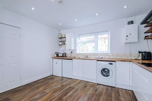 Cozinha moderna com armários brancos, máquina de lavar louça embutida, máquina de lavar roupa e janela com vista para o exterior.
