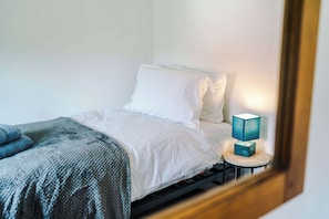 A single bed with white bedding, a grey knitted throw, and a teal-colored lamp on a bedside table. - Nottingham | Modern Home | Free Parking | Sleeps 5 (Beeston)