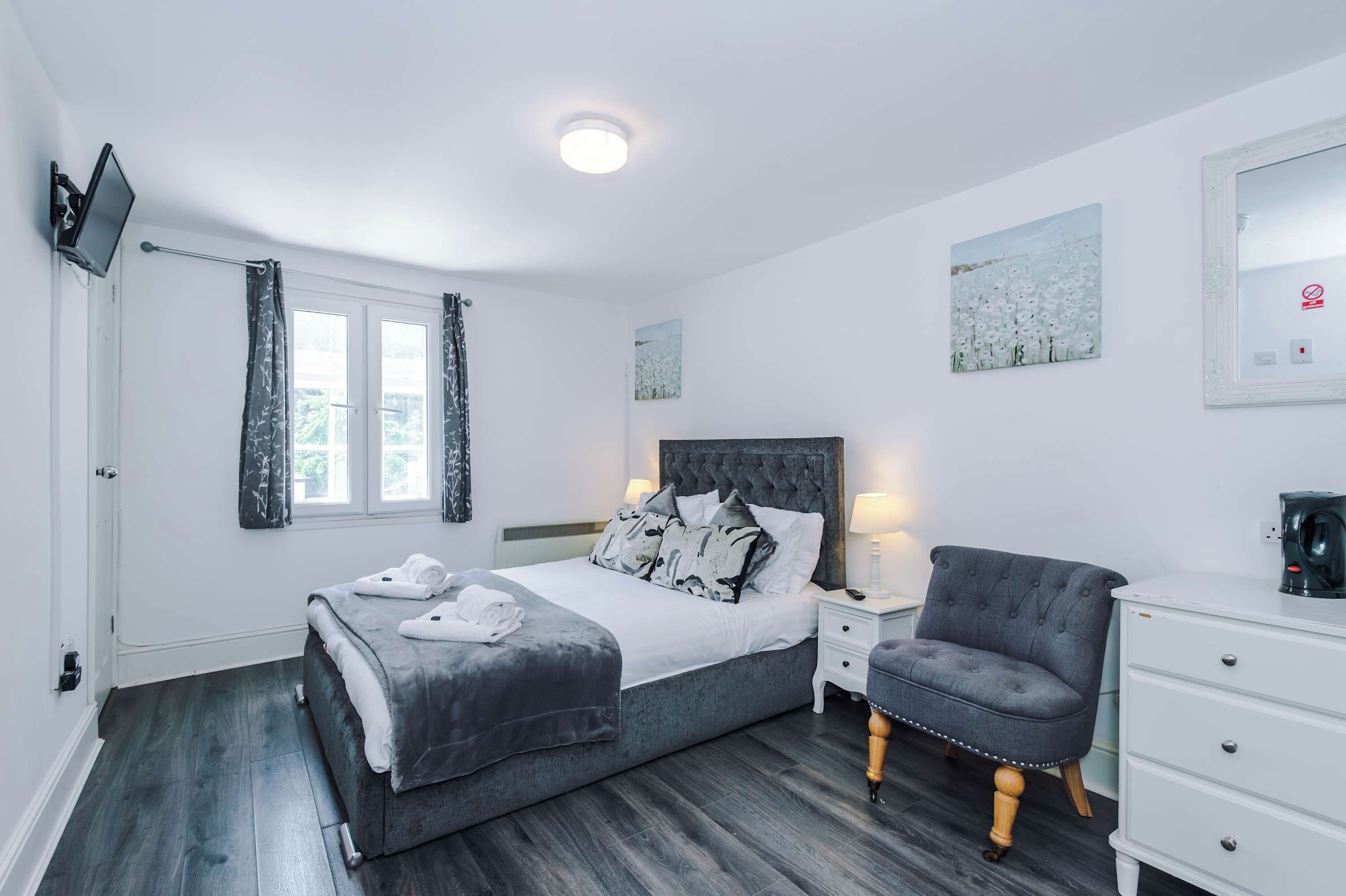 Ein Schlafzimmer mit Bett, Nachttischen, einem Sessel, einem Fernseher und Kunstwerken an den Wänden.