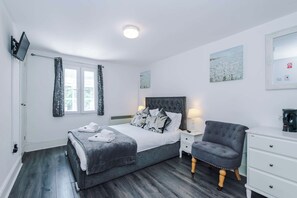 Quarto com cama, mesas de cabeceira, uma cadeira, televisão e obras de arte nas paredes.