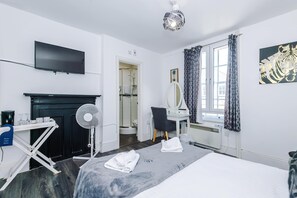 Une chambre d’hôtel équipée d’un lit, d’un téléviseur à écran plat, d’un ventilateur de plafond, d’une douche, d’une coiffeuse avec un miroir et d’une fenêtre avec des rideaux.