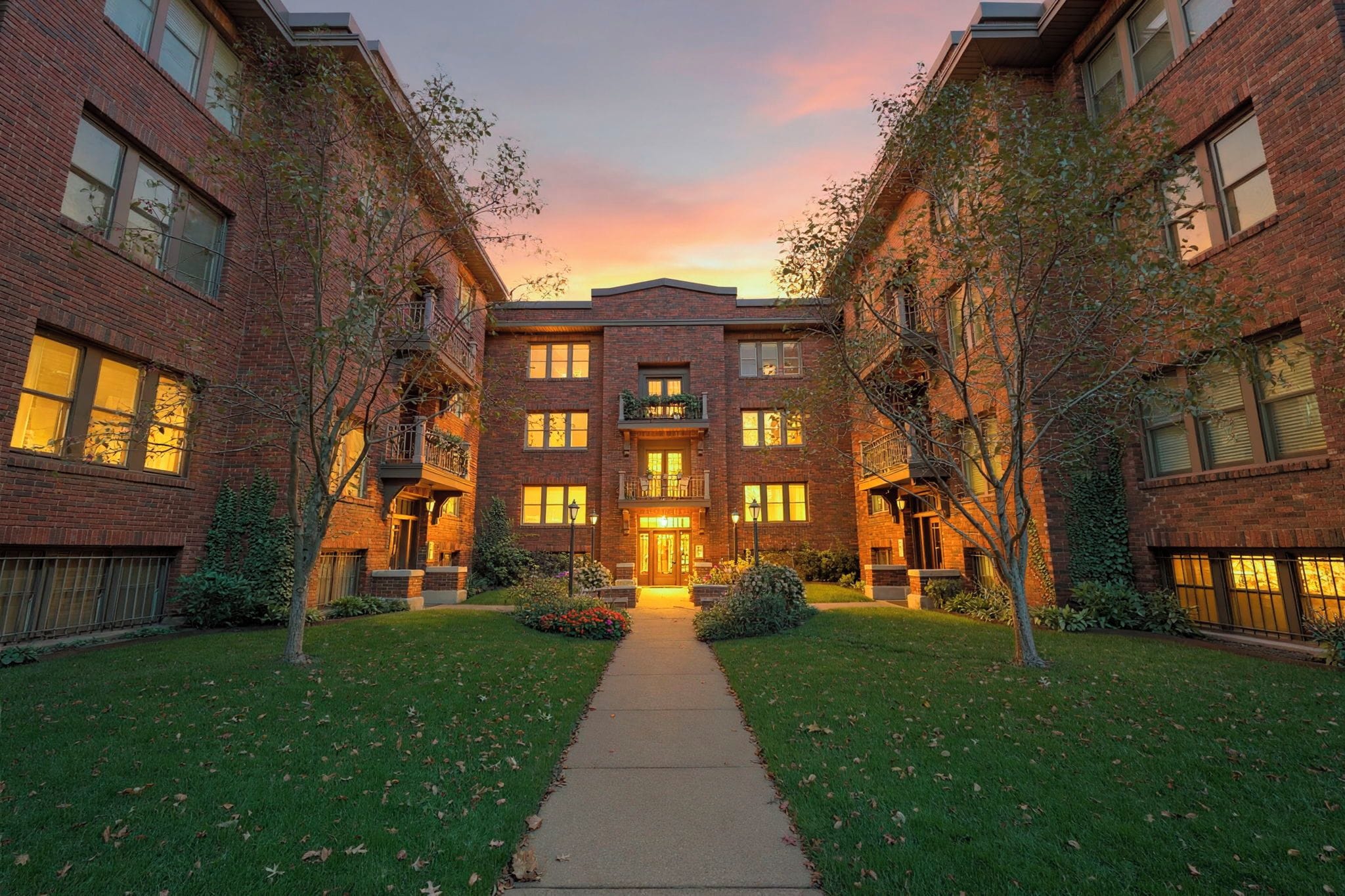 A multi-story brick building with a central entrance, surrounded by a pathway and greenery.
