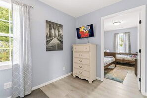 Une chambre à coucher avec un lit, une commode, un téléviseur et une fenêtre avec des rideaux.