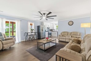 A living room with a sofa, a coffee table, and a dining area with a kitchen in the background. - White River Retreat Escape - Hot Tub, 5 BRs, 2 Homes (West Fork)