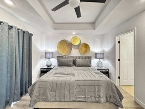 A bedroom with a bed, two bedside tables, a ceiling fan, and a door. - The Ultimate Fayetteville Retreat - Two Homes, 8 BRs, 5 Mi to U of A (Fayetteville)