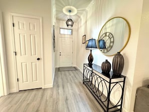 A hallway with a white door, a console table with two lamps and vases, a large mirror, and a ceiling fan. - The Ultimate Fayetteville Retreat - Two Homes, 8 BRs, 5 Mi to U of A (Fayetteville)