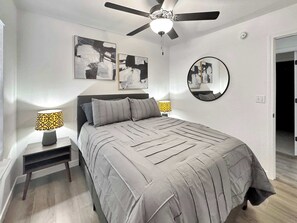 Un dormitorio con cama, dos lámparas de noche, un ventilador de techo y dos cuadros abstractos en la pared.
