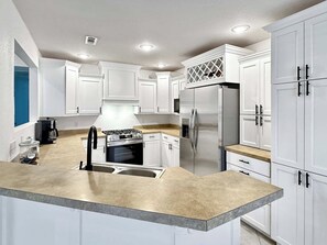 A modern kitchen with white cabinets, a stainless steel refrigerator, a gas stove, and a built-in oven. - The Ultimate Fayetteville Retreat - Two Homes, 8 BRs, 5 Mi to U of A (Fayetteville)