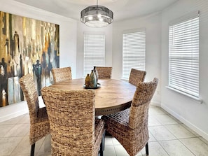 A dining room with a round table, wicker chairs, a chandelier, and a large abstract painting on the wall. - The Ultimate Fayetteville Retreat - Two Homes, 8 BRs, 5 Mi to U of A (Fayetteville)