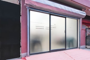 A storefront with a sliding glass door, a metal awning, and a red and black fence.