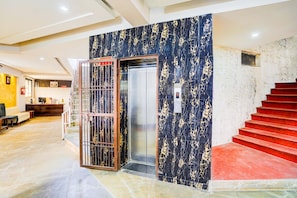 A hotel lobby with a reception desk, a staircase, and a digital elevator display.