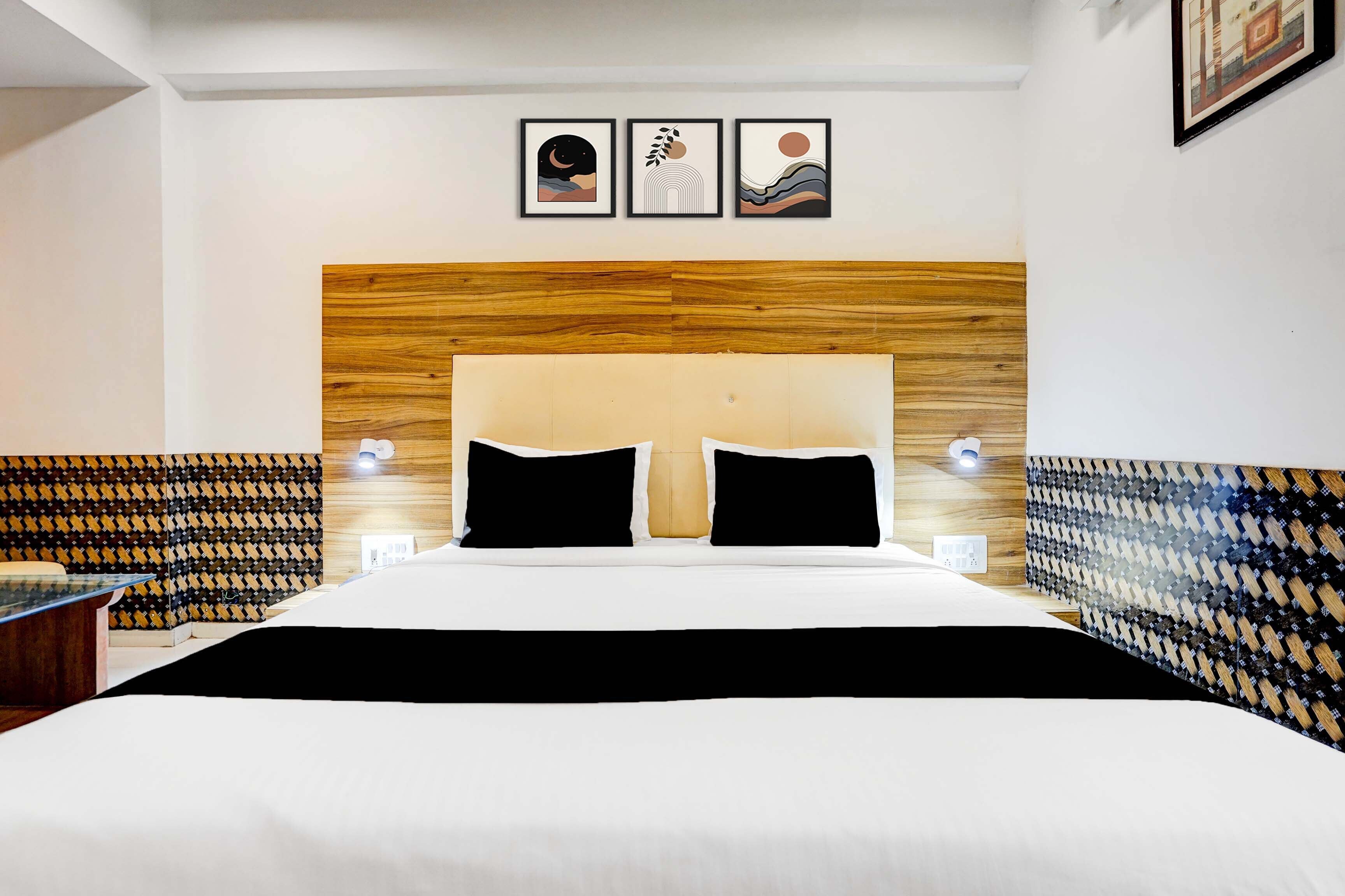Habitación de hotel con una cama grande, dos mesitas de noche con lámparas, un cabecero de madera y tres obras de arte enmarcadas en la pared.