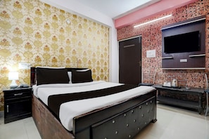 A bedroom with a bed, a nightstand, a lamp, a TV, and a wall with a patterned wallpaper. - Super Hotel O A.N College Patna (Patna)
