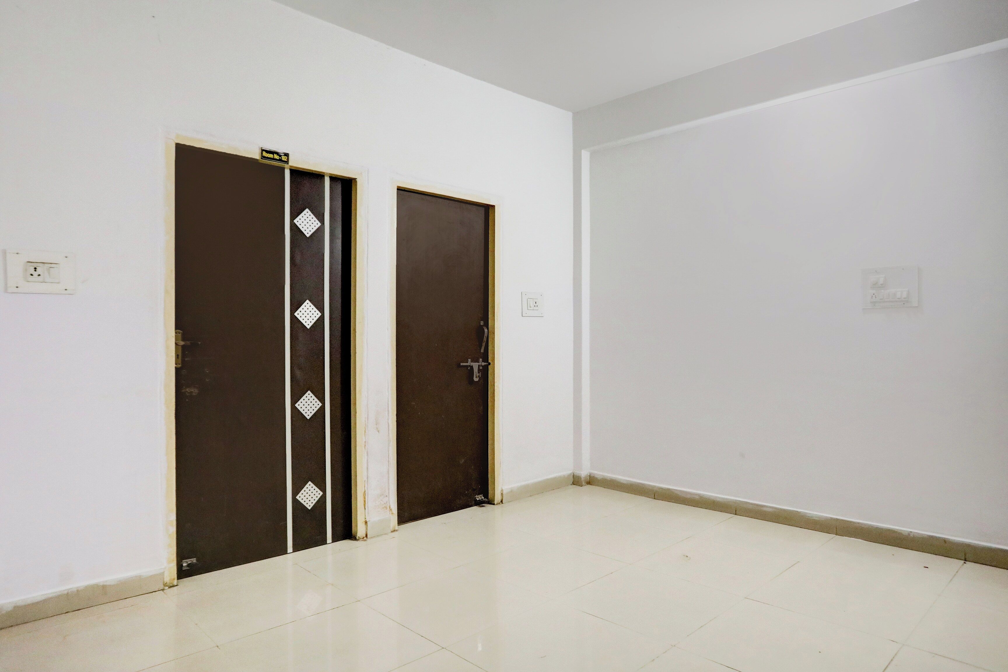 A room with two dark brown doors, white walls, and a tiled floor.