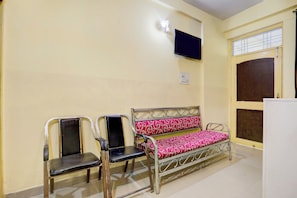 A waiting area with metal chairs and a bench, a flat-screen TV mounted on the wall, and a window with blinds. - Super Hotel O A.N College Patna (Patna)