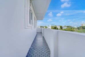 A narrow balcony with a patterned floor, white walls, and a clear view of the sky and distant buildings.