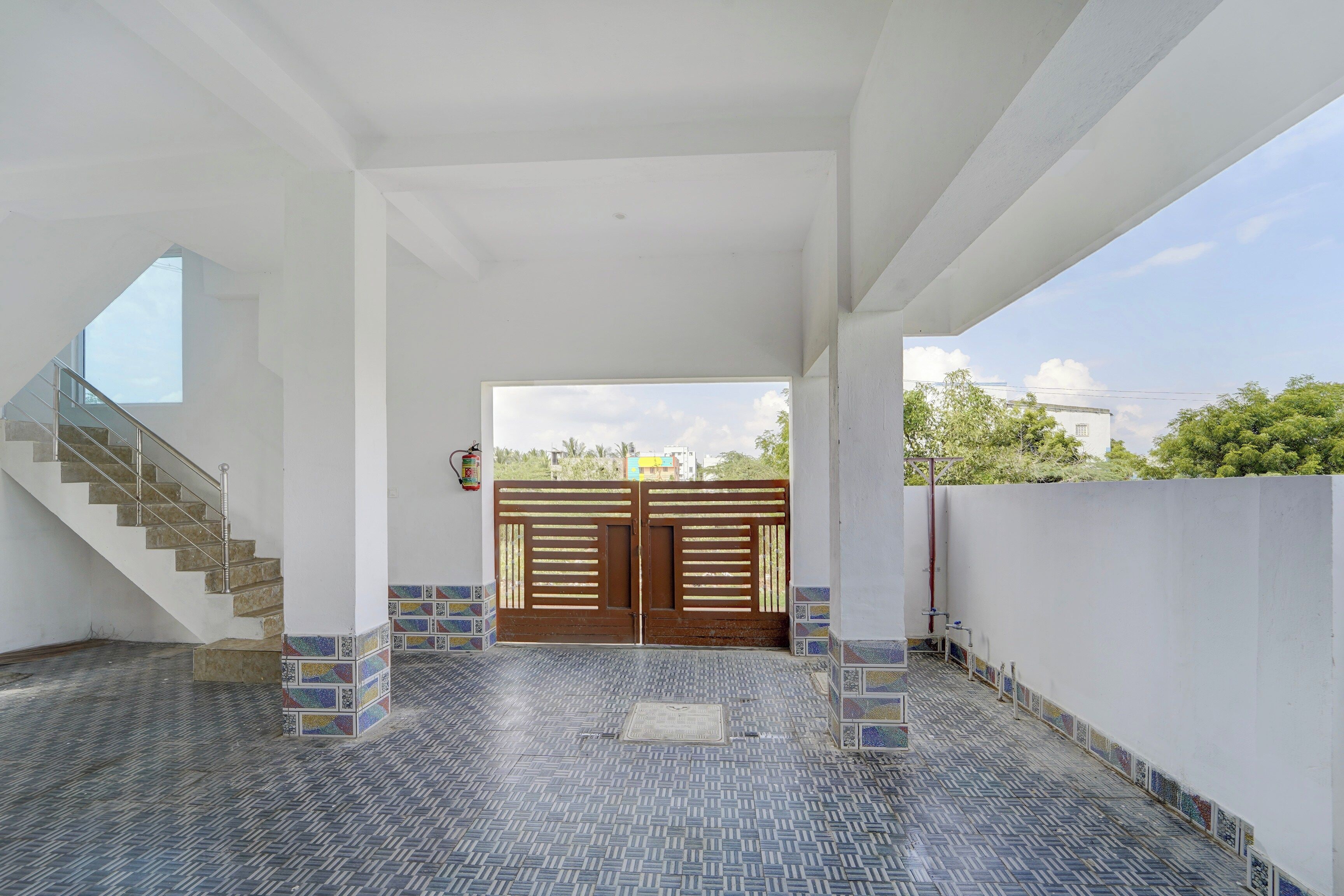 Un interior espacioso con una escalera, un gran portón y piso de baldosas.