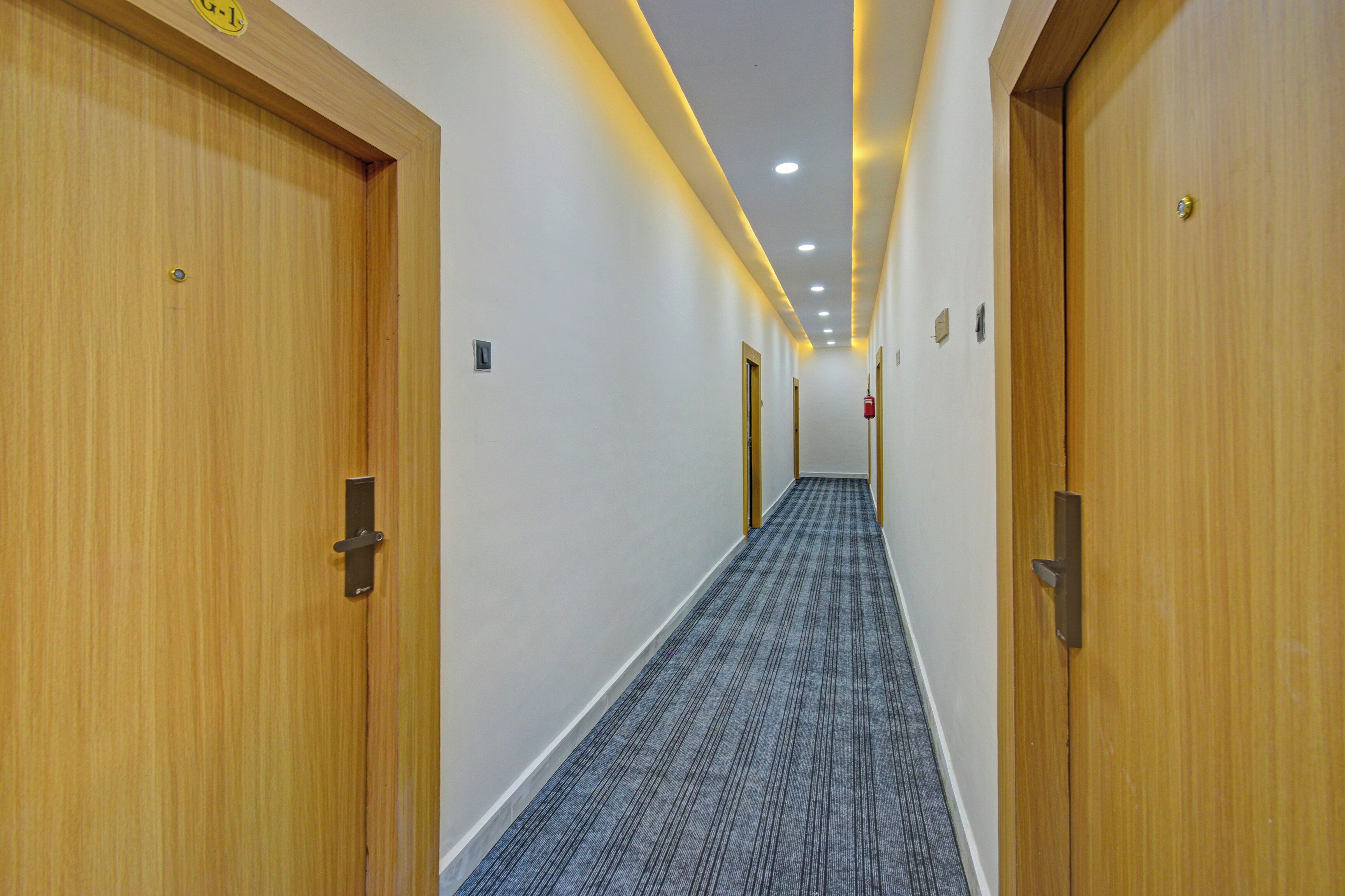 Un pasillo de hotel con puertas de madera, alfombra estampada e iluminación empotrada.