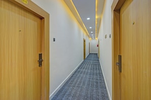 A hotel hallway with wooden doors, a patterned carpet, and recessed lighting.