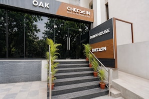 A hotel entrance with a staircase leading up to a check-in area, flanked by potted plants.