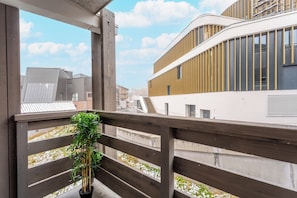 A balcony with a wooden railing, a potted plant, and a view of modern buildings. - Lauzieres (Les Belleville)