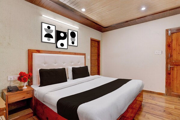 A bedroom with a bed, a nightstand, a vase with flowers, and a door. - Hotel O Vashisht Temple (Manali)