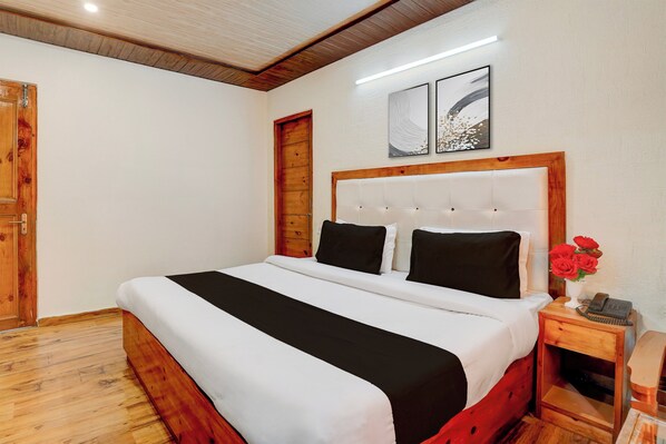 A bedroom with a wooden headboard, a bed with white and black bedding, a nightstand with a telephone, and two wall-mounted artworks.