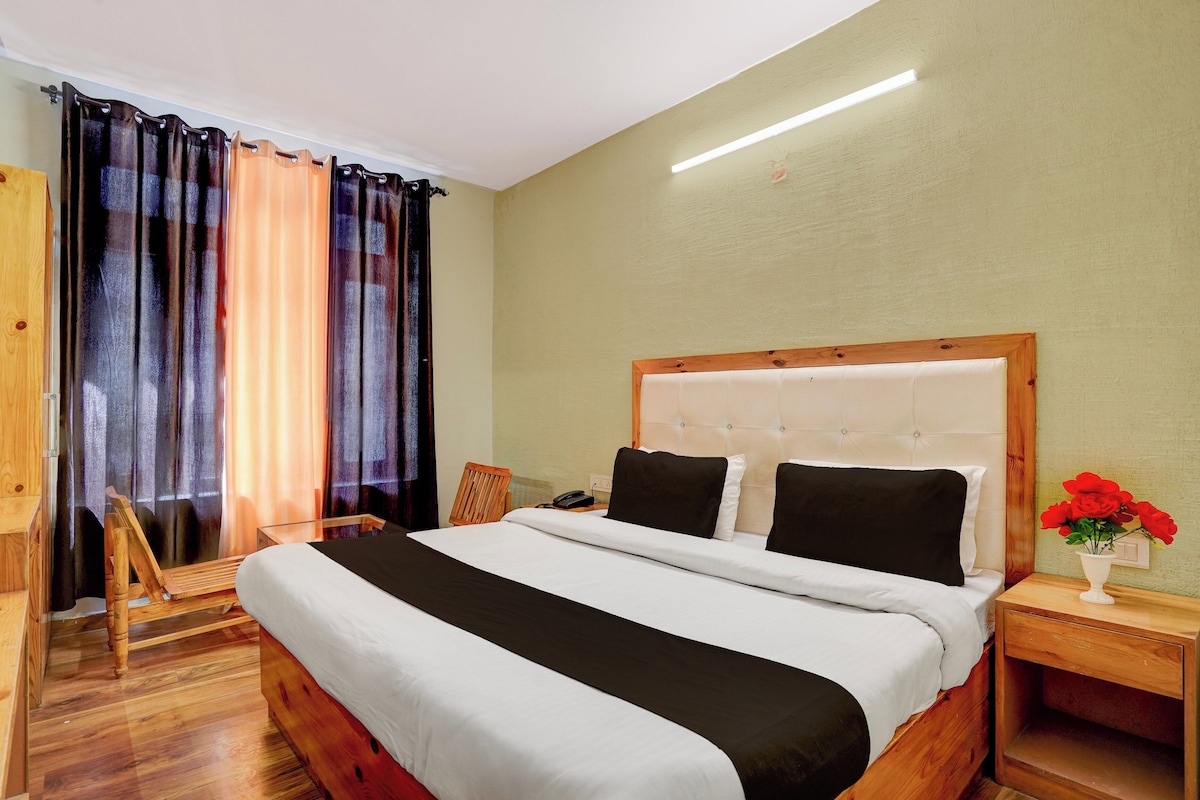 A hotel room with a bed, a bedside table, a chair, and a window with curtains.
