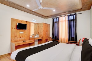 A hotel room with a bed, a desk, a television, and a window with curtains. - Hotel O Vashisht Temple (Manali)