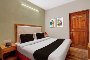 Quarto de hotel com uma cama, uma mesa de cabeceira de madeira, um telefone, uma luminária na parede e duas obras de arte emolduradas.