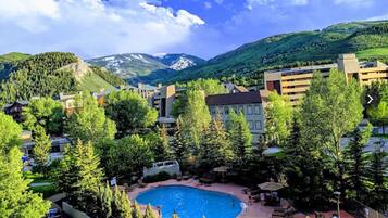 Un hotel con piscina rodeado de árboles y edificios, con montañas al fondo.